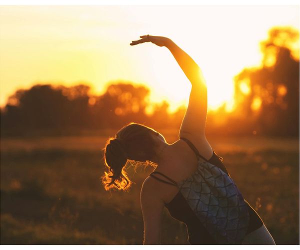 Happy active woman stretching outdoors during sunrise.